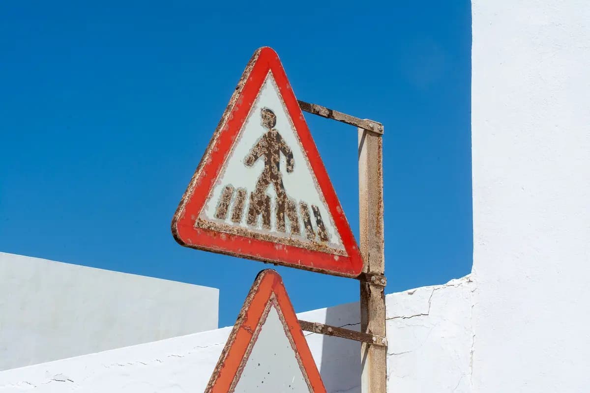 A weathered pedestrian crossing sign against a vivid blue sky, symbolizing caution and time.